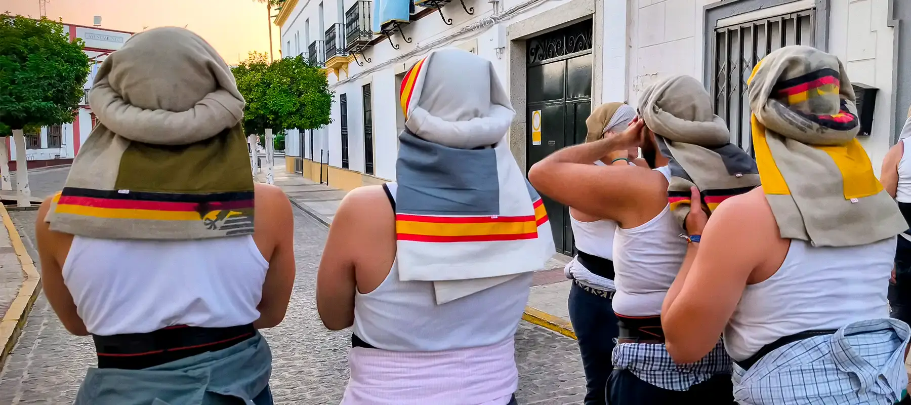 Cuadrilla de costaleros de espaldas en una calle encalada, cada uno con su costal de Rayas y Lunares